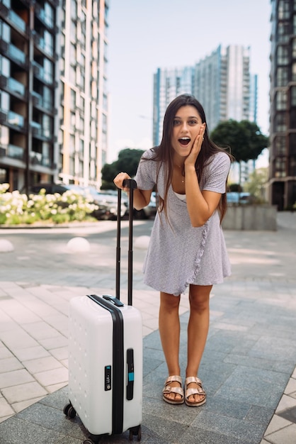 Femme élégante avec valise regardant la caméra