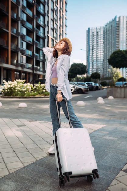 Femme élégante avec valise regardant la caméra