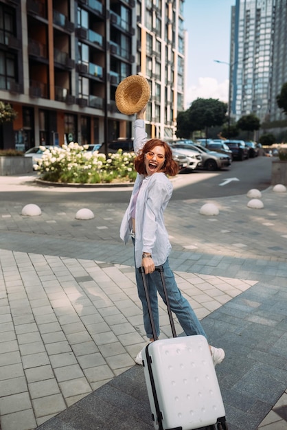 Femme élégante avec valise regardant la caméra