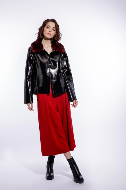 Femme élégante en veste de cuir noir pantalon pantalon rouge posant sur fond blanc