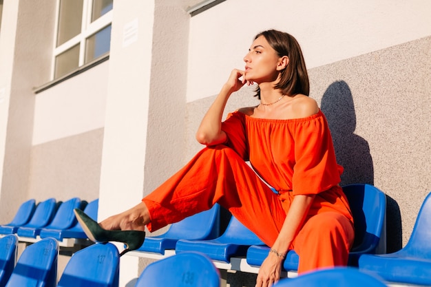 Femme élégante en vêtements orange au coucher du soleil au stade de piste cyclable posant