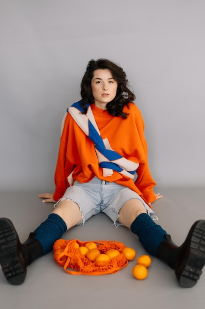 Femme élégante vêtue d'une veste en tricot orange posant pour une photo dans un studio photo sur un fond de papier gris Des émotions vives pose un concept moderne