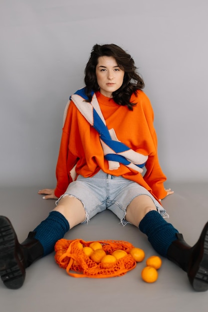 Femme élégante vêtue d'une veste en tricot orange posant pour une photo dans un studio photo sur un fond de papier gris Des émotions vives pose un concept moderne