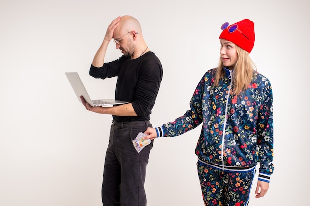 Femme élégante voler de l'argent à l'homme travaillant à l'ordinateur sur fond blanc