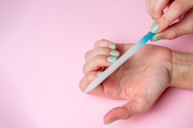 Une femme elle-même lime ses ongles avec une lime à ongles sur sa main sur fond rose. Soins des ongles des mains à la maison. Beauté et Santé. Espace de copie