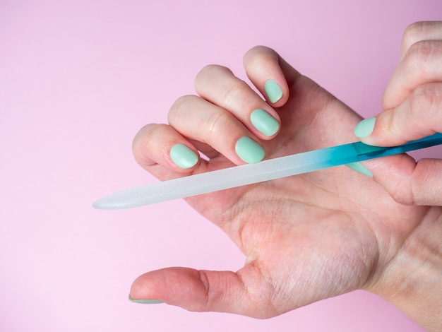 Une femme elle-même lime ses ongles avec une lime à ongles sur sa main sur fond rose. Soins des ongles des mains à la maison. Beauté et Santé