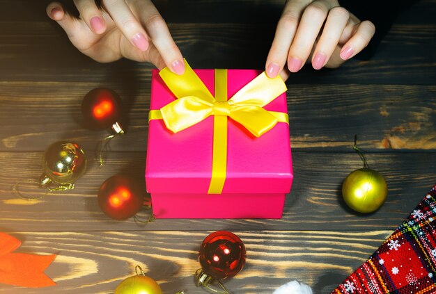 Une femme emballe des cadeaux de Noël. Félicitations aux amis et à la famille. Décorations sur table en bois. Salutations de bonne année. Ambiance chaleureuse et moment festif. Copiez le lieu de l'espace.