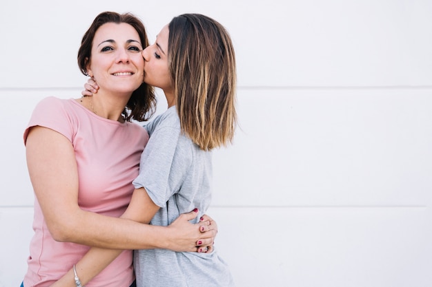 Photo femme embrassant une femme près d'un mur blanc