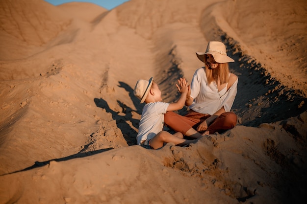 Photo femme embrassée par son fils aimant pendant le coucher du soleil. mère avec son fils sur une dune de sable. voyage.