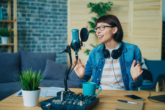 Femme émotionnelle parlant gesticulant enregistrement audio dans le microphone à la maison