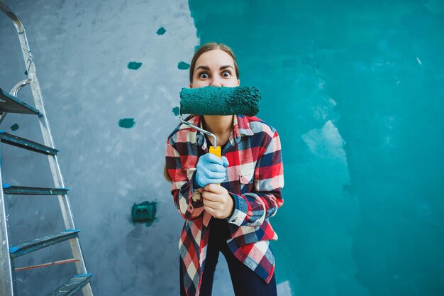 Une femme émotive peint les murs Jeune jolie femme souriante en chemise tenant un rouleau dans la main droite et chantant Réparation dans la chambre