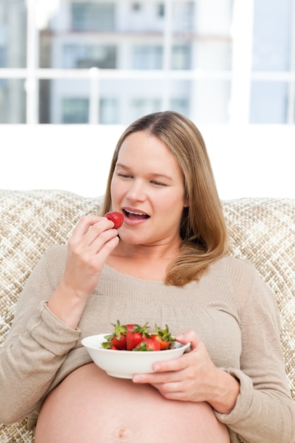 Femme enceinte affamée, manger des fraises assis dans le salon