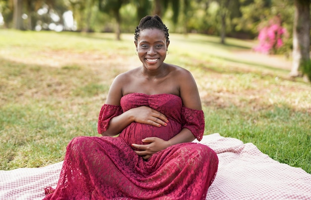 Femme enceinte africaine souriant à la caméra tout en touchant son ventre - Concept de maternité et de bonheur