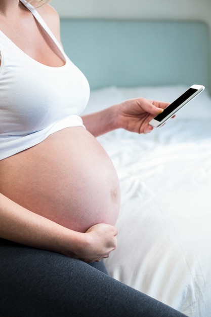 Femme enceinte à l&#39;aide de smartphone sur son lit