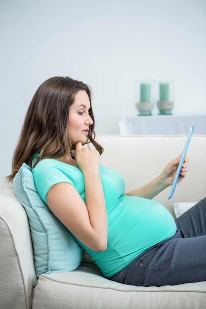 Femme enceinte à l&#39;aide d&#39;une tablette sur un canapé