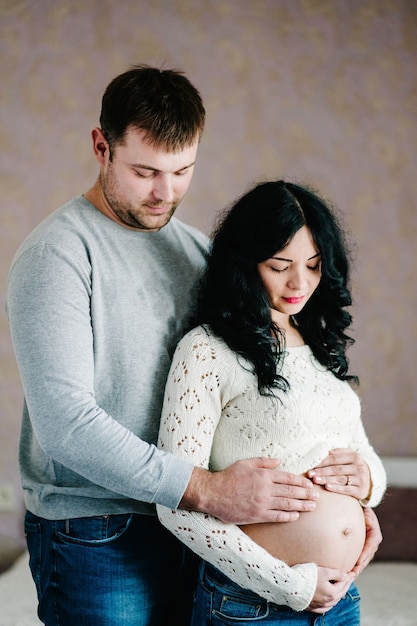 Femme enceinte et aimant bel homme étreignant le ventre à la maison.