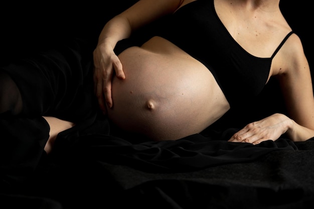 Femme enceinte allongée sur un drap noir touchant son beau ventre gonflé