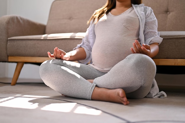 Femme enceinte asiatique détendue méditant dans sa pose de lotus de salon concentrant sa respiration