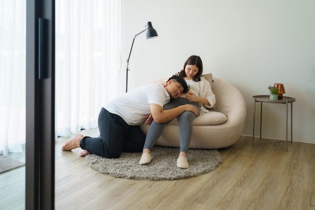 Une femme enceinte asiatique heureuse avec son mari qui attend un bébé à la maison et son mari essaie d'embrasser le bébé