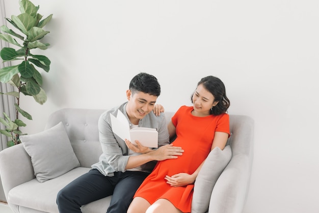 Femme enceinte asiatique et mari assis sur le canapé et livre de lecture