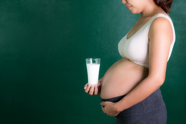 femme enceinte asiatique tenant un verre de lait avec un fond vert.