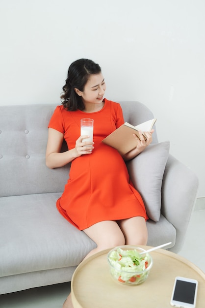 Femme enceinte asiatique tenant un verre de lait et livre de lecture