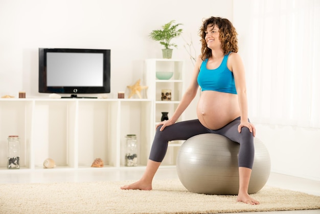 Femme enceinte assise sur le ballon de fitness et relaxante.