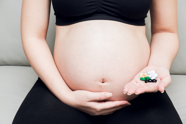 Femme enceinte assise sur un canapé et main tenant des pilules de médecine.