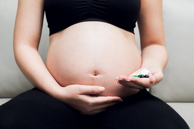 Femme enceinte assise sur un canapé et main tenant des pilules de médecine.