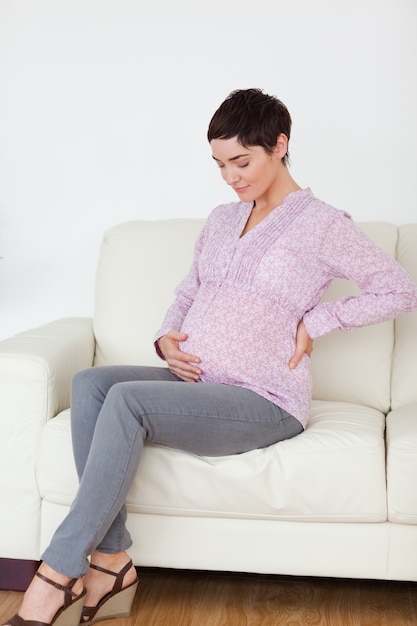 Femme enceinte assise sur un canapé en touchant son ventre