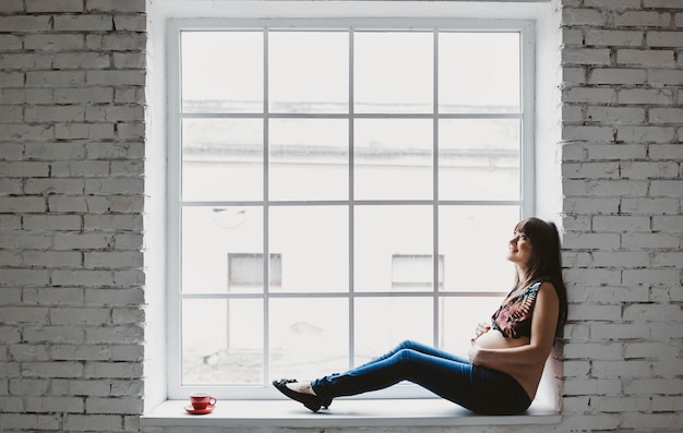 Photo femme enceinte assise dans le cadre de la fenêtre