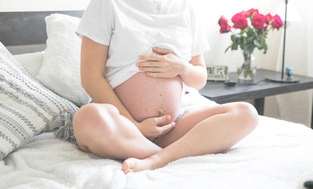 Femme enceinte assise sur un lit tenant Le concept de grossesse, de maternité et de soins prénataux Maman avec une nouvelle vie