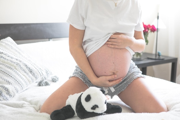 Femme enceinte assise sur un lit tenant Le concept de grossesse, de maternité et de soins prénataux Maman avec une nouvelle vie