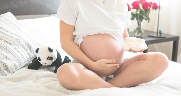 Femme enceinte assise sur un lit tenant Le concept de grossesse, de maternité et de soins prénataux Maman avec une nouvelle vie