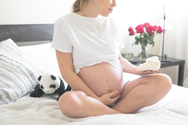 Femme enceinte assise sur un lit tenant Le concept de grossesse, de maternité et de soins prénataux Maman avec une nouvelle vie