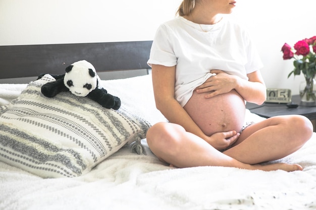 Femme enceinte assise sur un lit tenant Le concept de grossesse, de maternité et de soins prénataux Maman avec une nouvelle vie