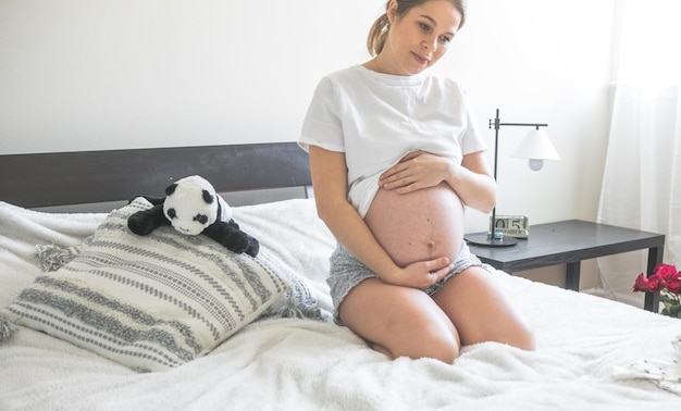 Femme enceinte assise sur un lit tenant Le concept de grossesse, de maternité et de soins prénataux Maman avec une nouvelle vie