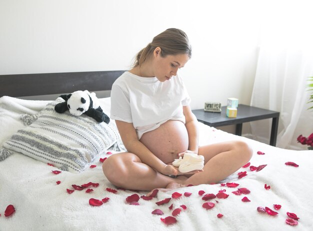 Femme enceinte assise sur un lit tenant Le concept de grossesse, de maternité et de soins prénataux Maman avec une nouvelle vie