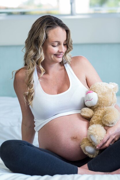 Femme enceinte assise avec un ours en peluche sur son lit