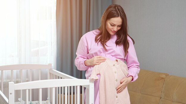 La femme enceinte attend le bébé et tient des vêtements de bébé