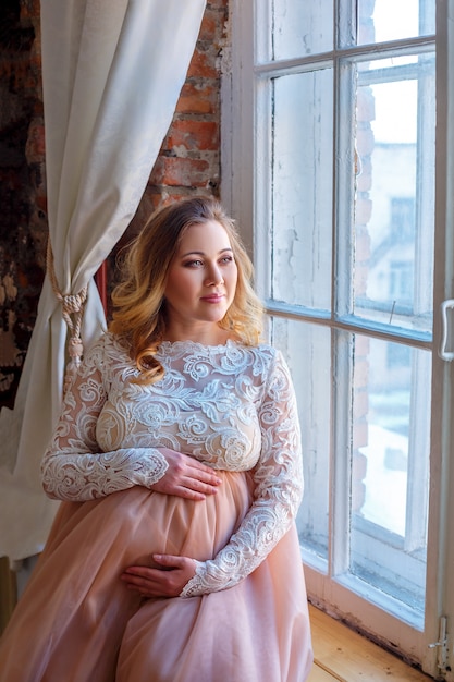 Femme enceinte attendant à la fenêtre, dans une belle robe, maternité