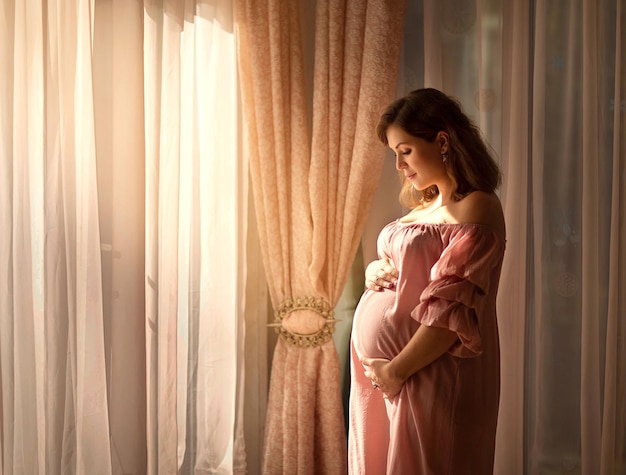 Une femme enceinte attendant son premier enfant se tient à la fenêtre
