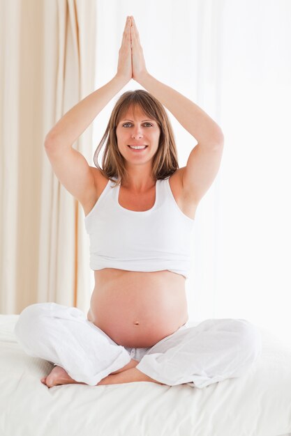 Femme enceinte attrayante, faire du yoga sur un lit