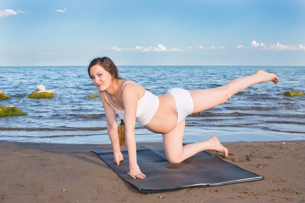 Femme enceinte aux cheveux longs méditant dans une pose de yoga sur la mer