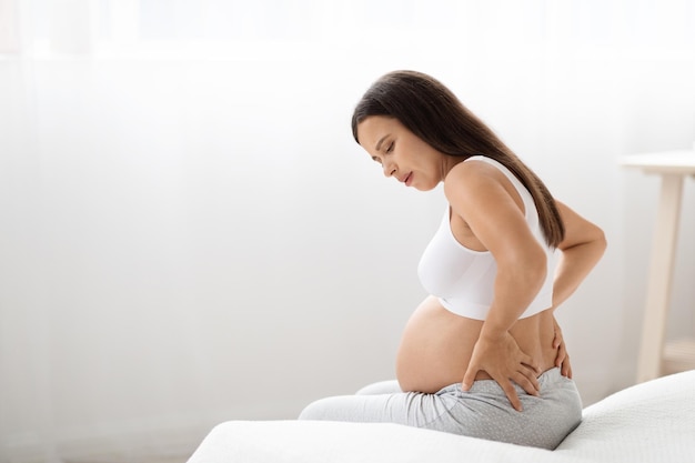 Femme enceinte ayant mal au dos assis sur le lit à la maison