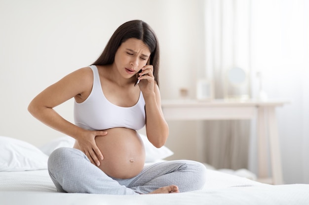 Femme enceinte bouleversée ressentant de la douleur et de l'inconfort appelant un médecin