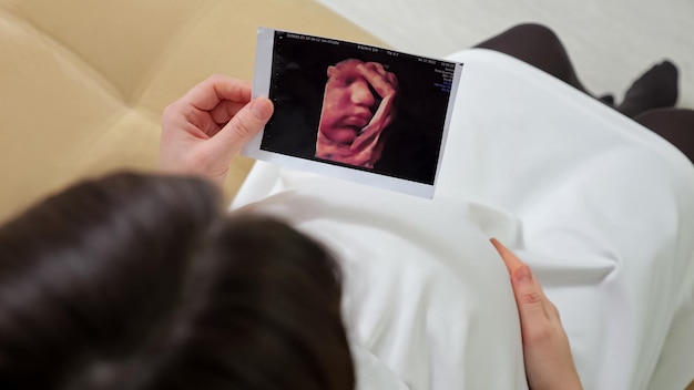 Une femme enceinte caresse le ventre et regarde une photo échographique