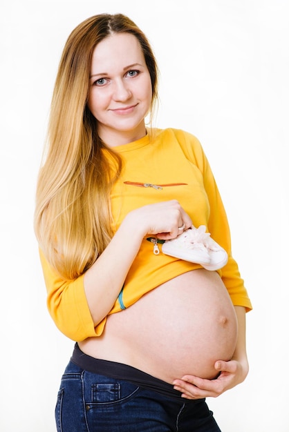 Femme enceinte caucasienne tenant un peu de chaussures sur son ventre isolé sur blanc