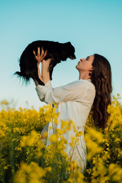 Une femme enceinte avec un chien noir se tient dans un champ de colza