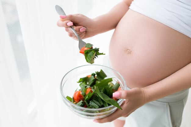 La femme enceinte commence à manger de la salade fraîche dans un bol en verre. Concept d'alimentation saine, de corps et de soins de santé de la période spéciale de la future mère